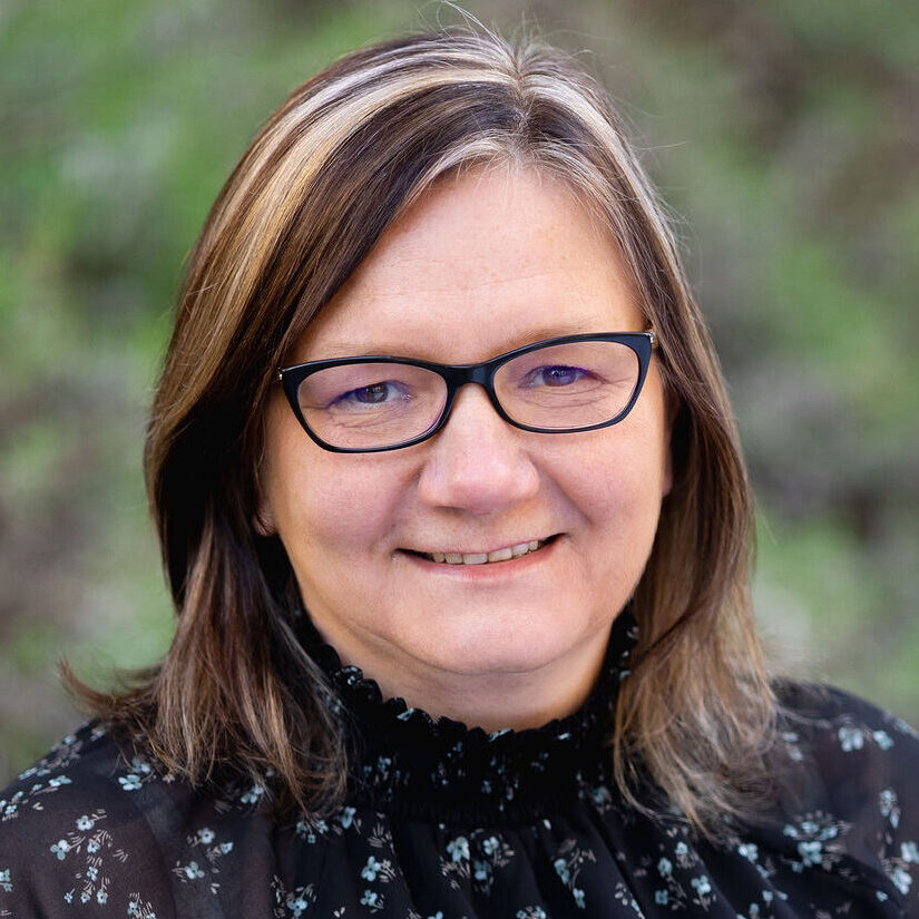 Headshot of Nicole Jeschelnik. She has midlength brown hair, and is wearing black rimmed glasses and a dark printed top.