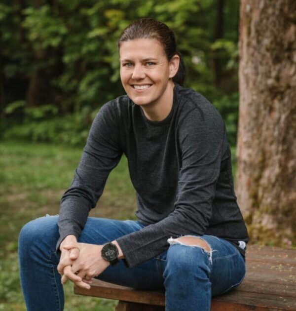 A person smiling is pictured outside, sitting on a wooden bench.