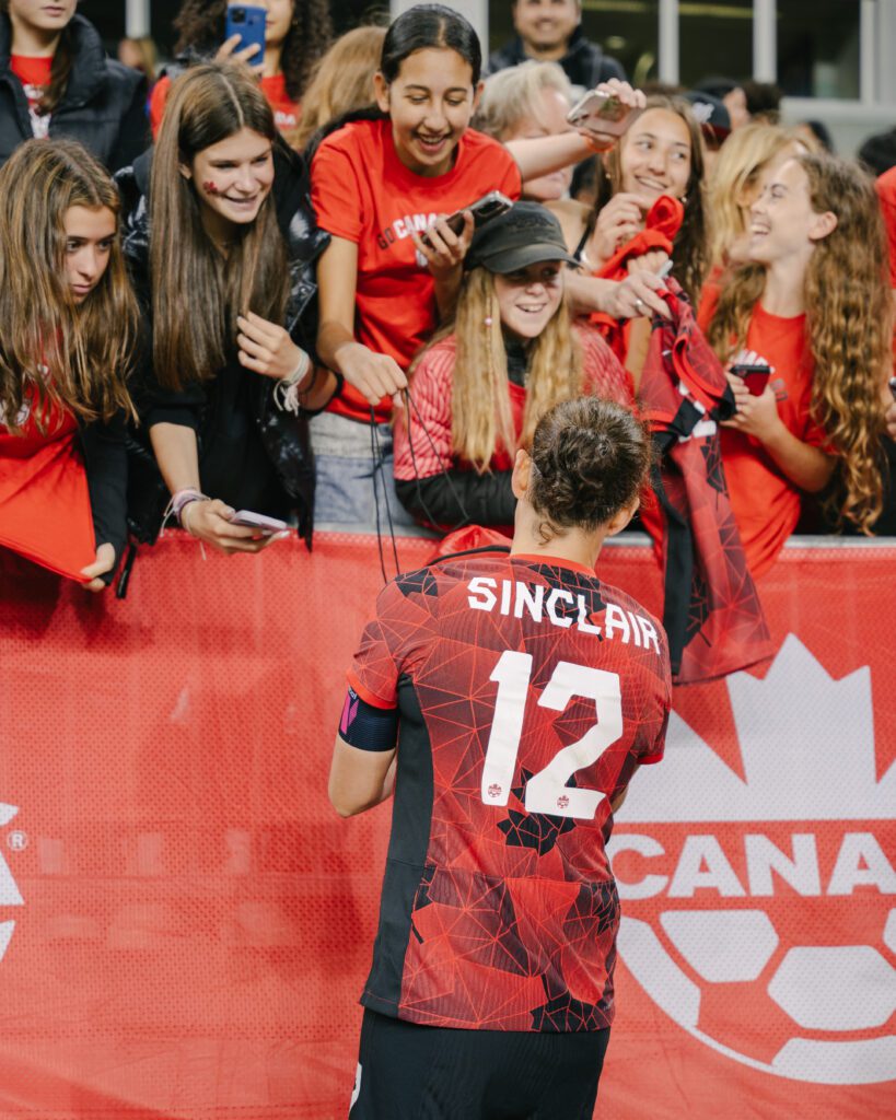 An athlete is pictured standing in front of a crowd of fans, signing autographs.